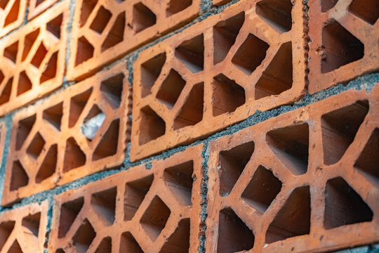 Terracotta roster brick wall texture background with geometric breeze blocks. Red clay ventilation bricks pattern template under bright afternoon sunlight.