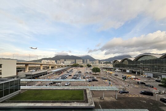 View of Hong Kong International Airport terminal buildings, parking lot and aircraft taking off.