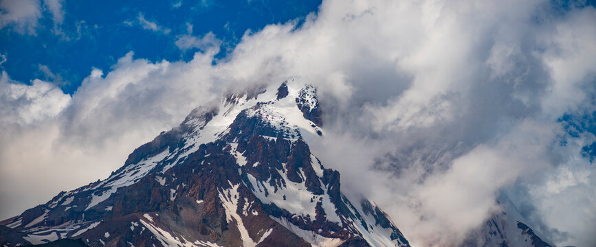 Dramatic snowy Kazbek mountain peak wrapped in thick clouds with copy space