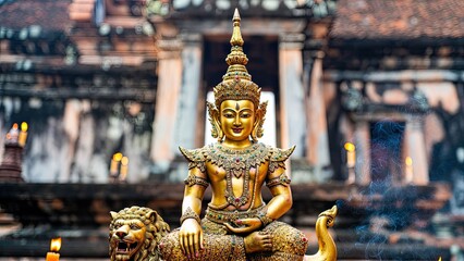 Fototapeta premium Golden statue of a deity on a lion base at a historic temple with incense smoke in the background