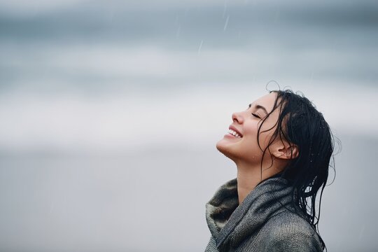 Happy individual enjoying the rain on the beach with eyes shut and a big smile on their face