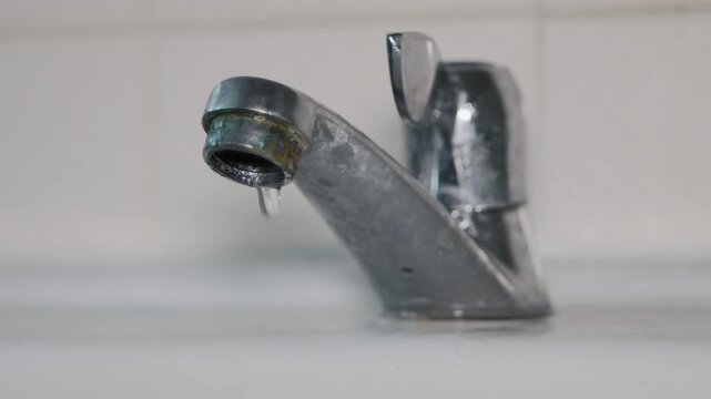 Close-up of water leaking from an old metal tap. Concept of plumbing problems, water waste, home maintenance, and the need for repair.