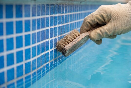 Manual scrubbing of blue swimming pool mosaic tile border