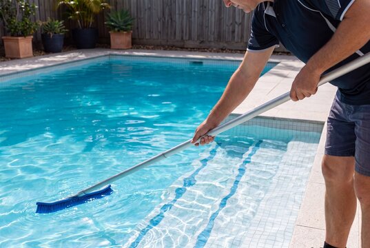Worker cleaning residential swimming pool floor with brush