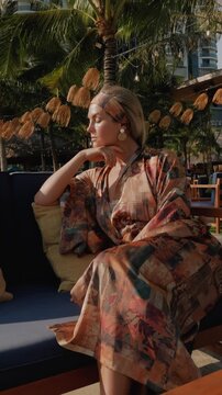 Relaxed woman in patterned beach kimono enjoying sunshine at tropical resort lounge  