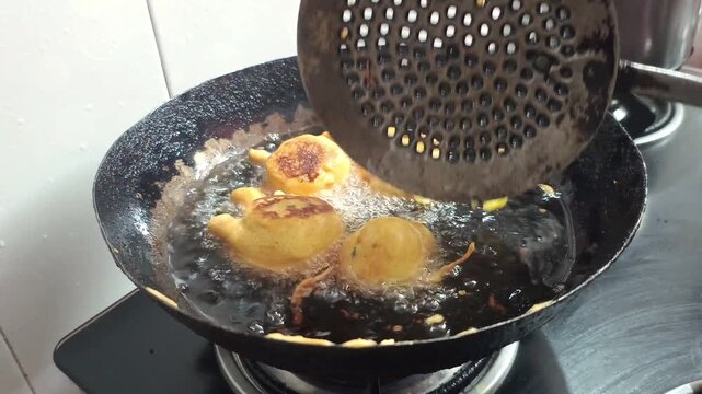 Close up of frying traditional Indian batata vada or aloo bonda pakora in hot oil