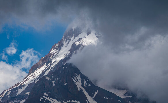 Dramatic snowy Kazbek mountain peak wrapped in thick clouds with copy space