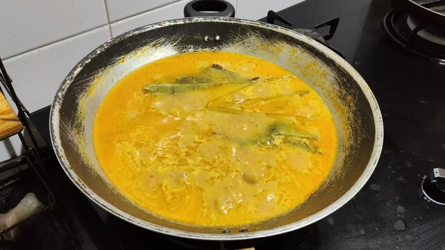 footage of yellow curry cooking in a wok with steam rising.