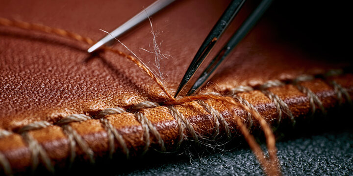 Close-up of a needle stitching brown leather with thread