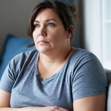 Pensive sad overweight obese woman sitting at her bedroom looking away very worried	
