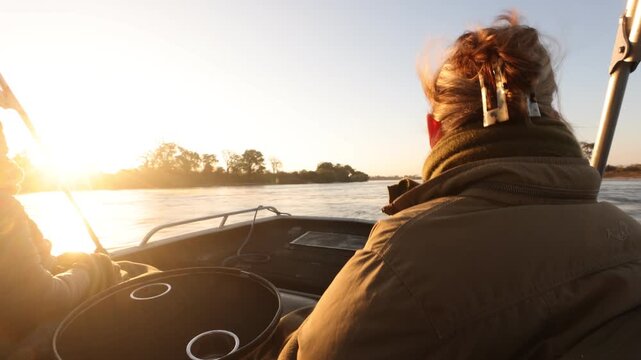 woman experiencing cold sunrise on the Zambezi River, as fog rises from the water, Zimbabwe, Africa