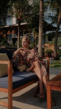 Relaxed woman in patterned beach kimono enjoying sunshine at tropical resort lounge  