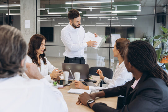 Businessman presenting financial data while multinational colleagues discuss marketing strategy in a modern office