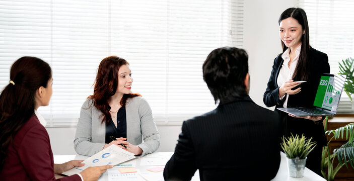 Asian businesswoman presenting ESG report on laptop to diverse team.