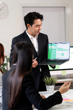 Asian businessman presenting ESG report on laptop screen to colleagues.