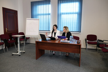 Fototapeta premium Two businesswomen work at a conference table, discuss documents, a laptop, and the results of financial analysis.