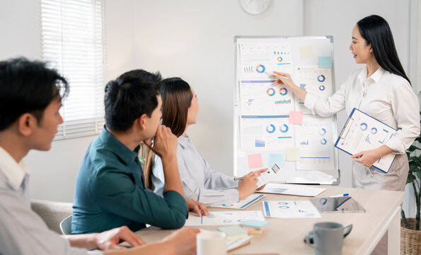 Asian businesswoman presenting financial charts on whiteboard to her team.