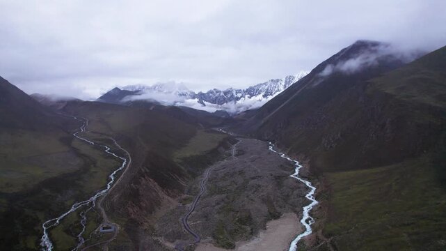Drone view of Baimalincuo lake in Mount Kula Kangri above from clouds, blue lake and white stream with snow capped mountain background. 4k real time footage travel concept b roll shot.