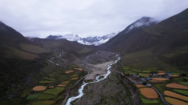 Drone view of Cuoyu village in Mount Kula Kangri, colorful farm field and white stream in valley with snow capped mountain background. 4k real time footage travel concept b roll shot.