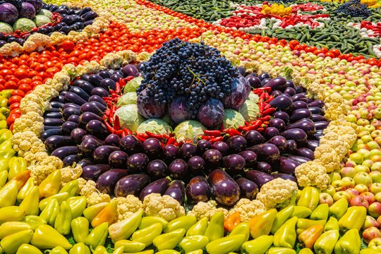Decorative spiral arrangement of fresh eggplants, tomatoes, grapes and zucchini at Tajik harvest festival market display