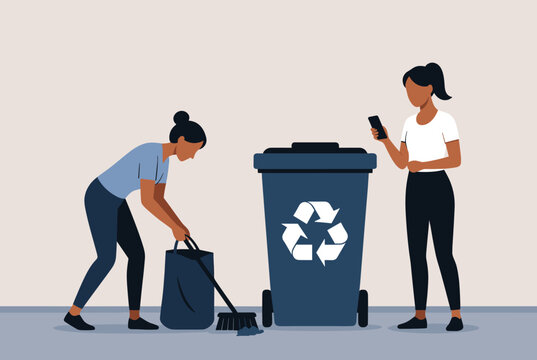 One woman sweeps and cleans trash while her colleague ignores her by looking at her smartphone near a recycling bin.