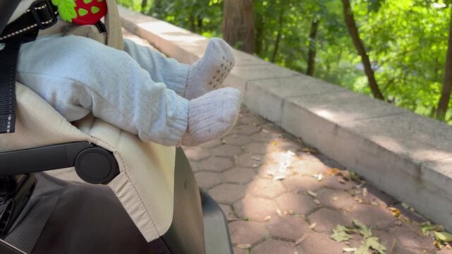 a baby's legs and feet, clad in light blue sweatpants and soft grey socks, dangling comfortably from a beige stroller.