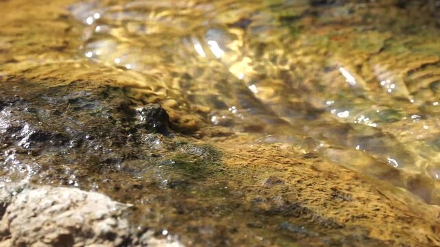 the view of a small natural stream or water puddle flowing through cracked and weathered brown stone boulders, showcasing detailed geological textures.