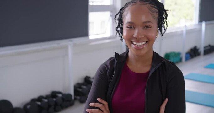 Adult African woman arms-crossed in maroon by dumbbells, smiling and laughing while camera zooming