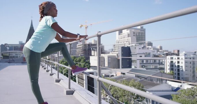 Woman in sportswear placing right foot on rooftop railing, leaning, stretching leg, warming up