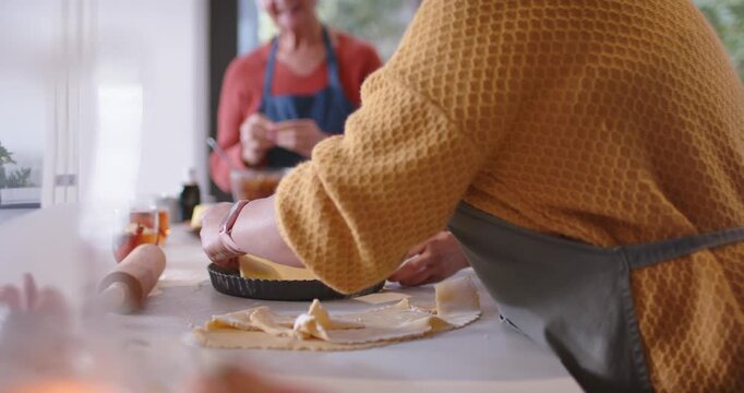 Diverse female friends placing tart pan on pastry, fitting crust and prepping filling for baking