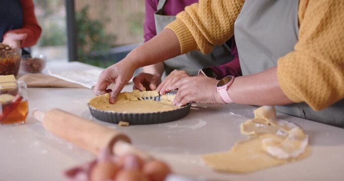 Diverse female bakers pressing crimping tart crust from pastry at counter in fluted pan for baking
