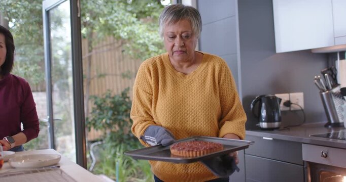 Diverse women hearing oven timer, Asian woman pulling tart onto island cooling rack for tea