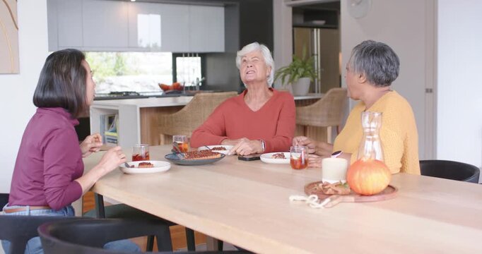 Diverse female kin sitting at table right woman offering fork senior replying, gesturing near phone