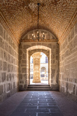 Fototapeta premium Historic stone corridor in the old town of Arequipa leading toward a sunlit courtyard with ornate colonial architectural details