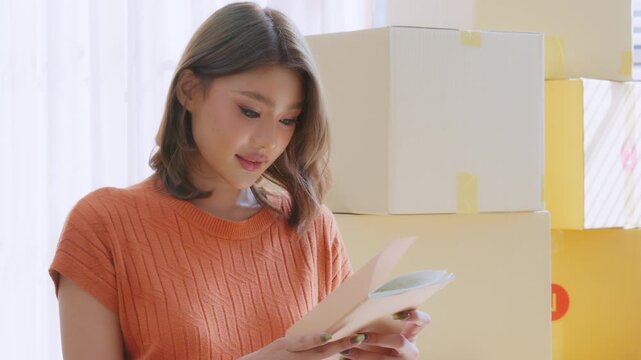 Young Asian woman happy and smiling unpack boxes at new house, relocation and people in real estate or apartment. Moving house concept