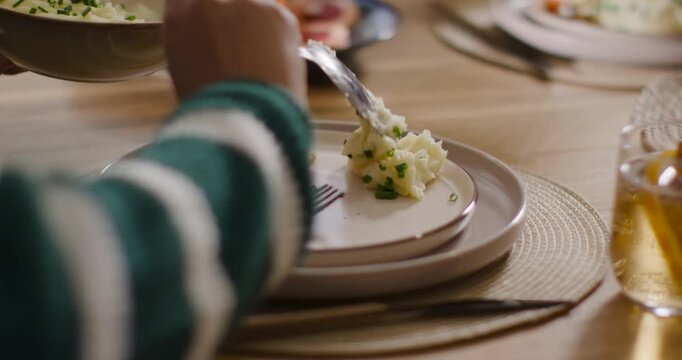 Female moving spoon into frame, scooping mashed potatoes onto plate for family meal at home table