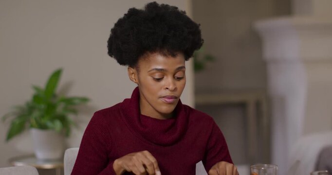 Woman in burgundy sweater cutting food with knife and fork at dining table hearing voice responding