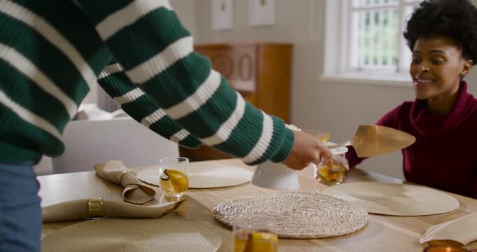 Diverse female friends watching woman entering left with server placing pie on stand to serve