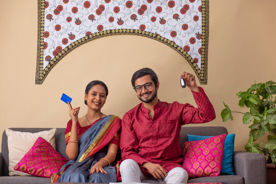Portrait of happy young couple sitting in living room with credit card and new car key
