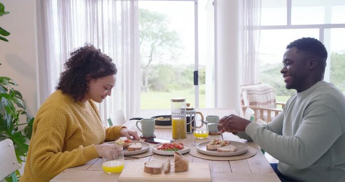 African American couple holding hands at wooden table, plates being set, reaching, eating together