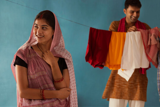 Portrait of woman with headscarf standing and her husband hanging clothes on clothesline