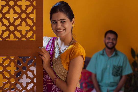 Portrait of smiling Gujrati woman standing and her husband sitting behind