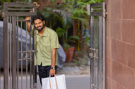 Young man standing at entrance gate with a shopping bag