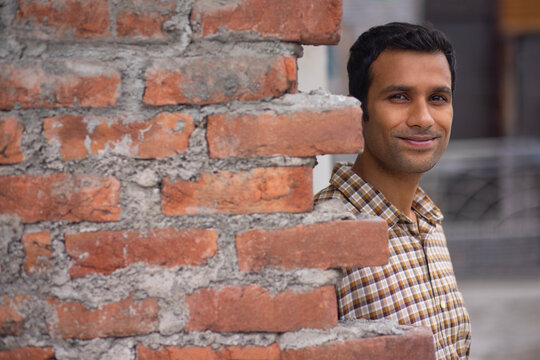 Portrait of young man standing behind brick wall