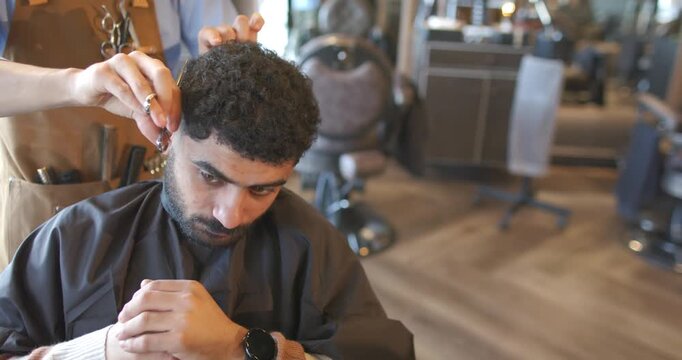 African American man in barber chair, barber lifting hair and trimming line with scissors to shape