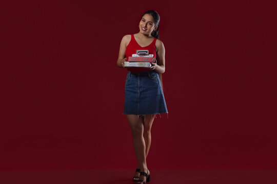 Teenage girl standing with gift boxes against maroon background