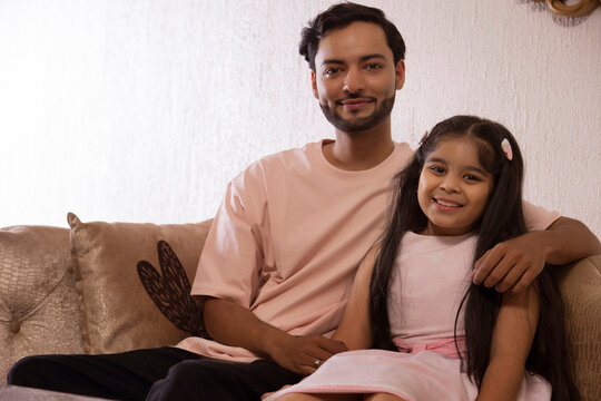 Father and daughter looking at camera while sitting together on sofa at home