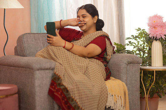 Happy woman having video call on mobile phone while relaxing on sofa at home