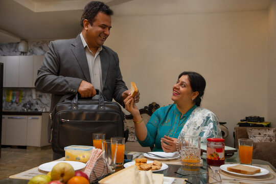 Woman giving slice bread with jam to her husband before going to office