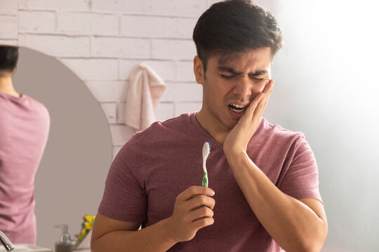 Young man suffering from toothache while brushing